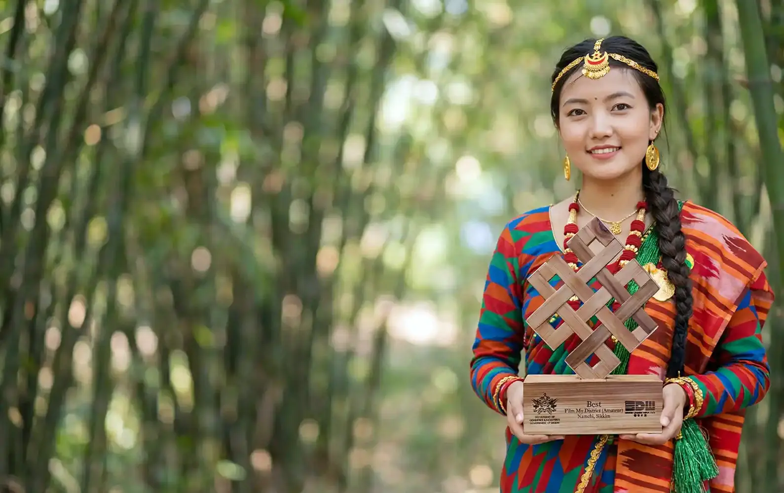 Woman in traditional Sikkimese attire holding a handcrafted wooden award in a bamboo grove in Sikkim